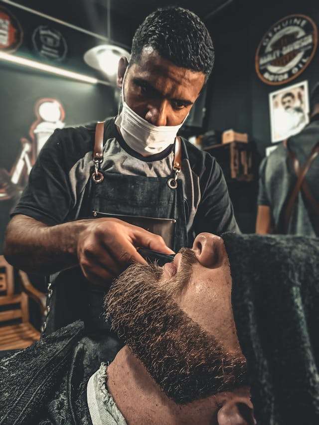 Barber at Bay State Barbershop in Norwood, MA trimming a client’s beard with precision.